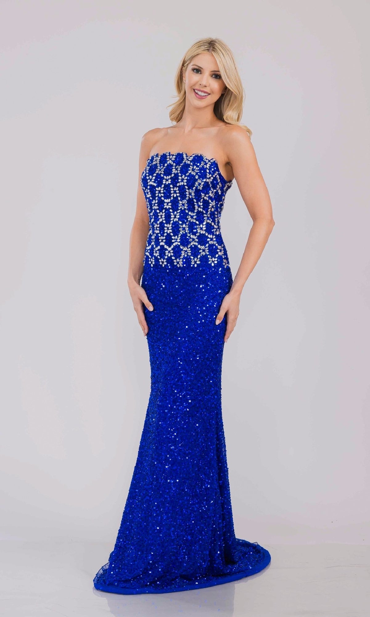 Woman wearing a royal blue strapless evening gown with a beaded patterned bodice on a light gray background